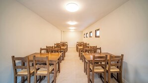 A conference room with multiple wooden tables and chairs, recessed ceiling lights, and small windows on the right wall. - Aran Hostel (Naut Aran)