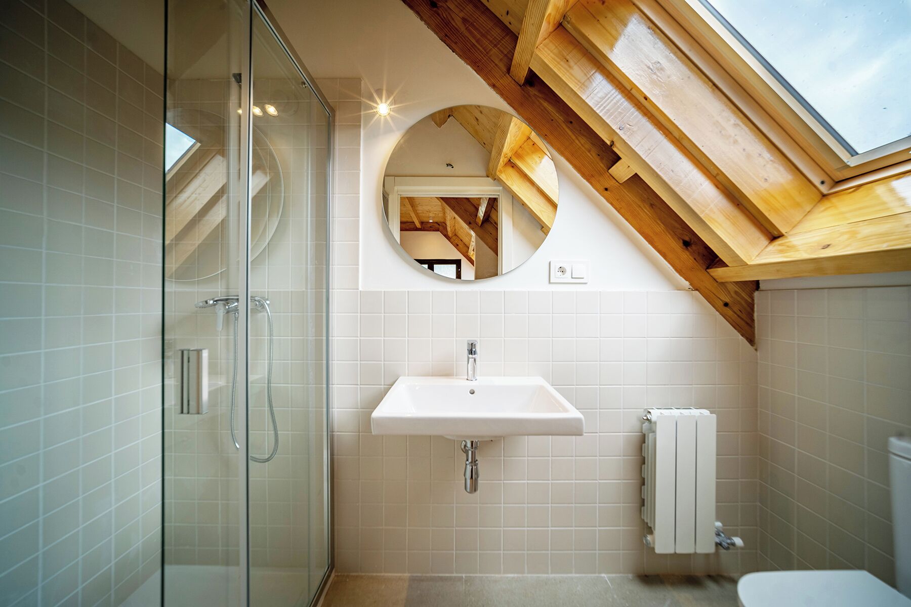 A modern bathroom with a glass-enclosed shower, a white sink, and a skylight above.