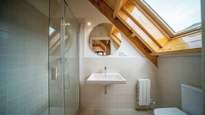 A modern bathroom with a skylight, glass shower enclosure, and a white sink. - Aran Hostel (Naut Aran)
