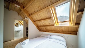 A bedroom with a wooden ceiling and a skylight, a bed, and a bathroom with a mirror and sink. - Aran Hostel (Naut Aran)