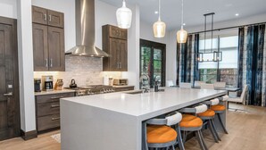 A modern kitchen with a large island, bar stools, and pendant lighting. - Vail Chalet | Platinum-Rated 4BR Luxury Home, Cascade (Vail)