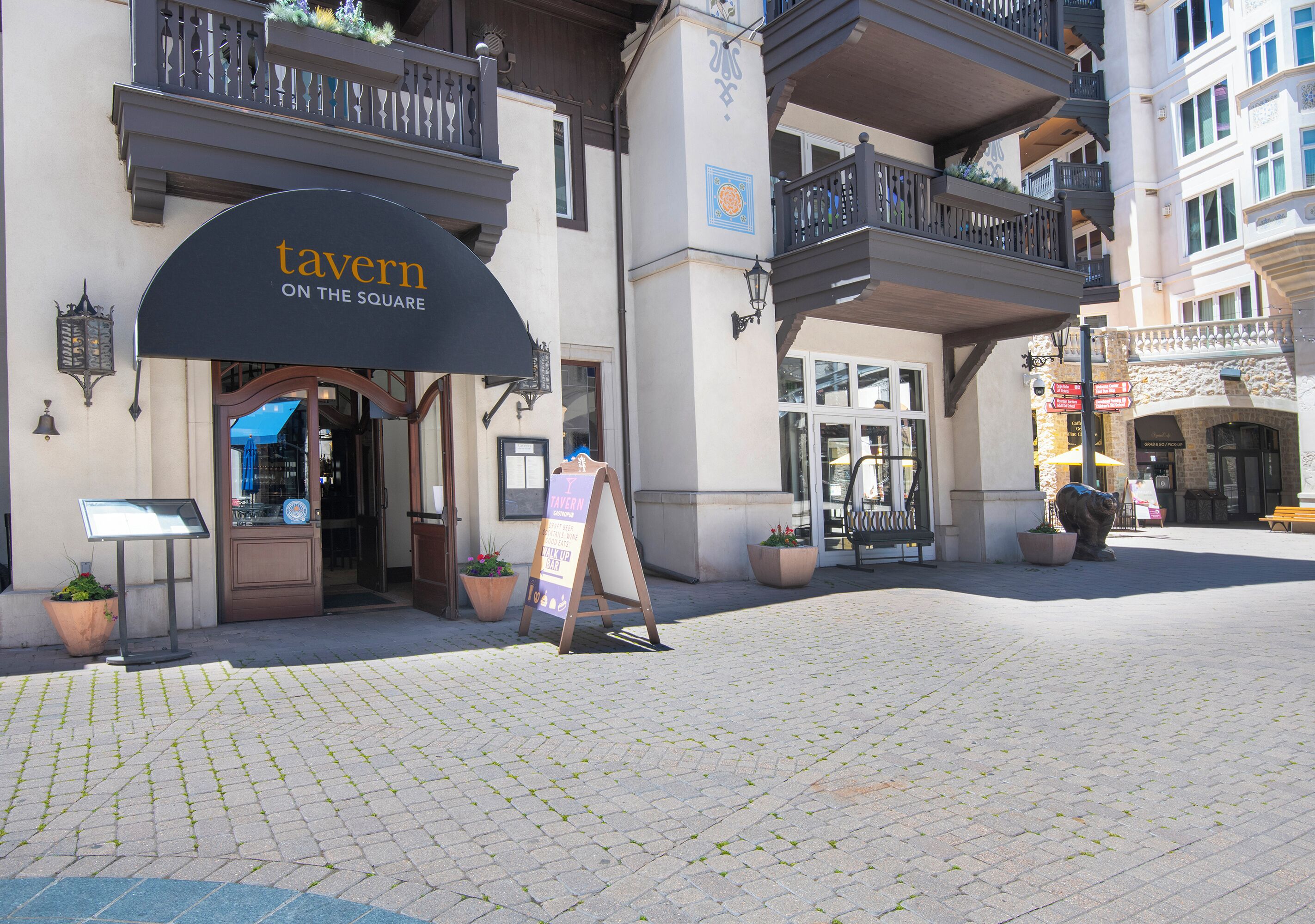 A tavern with a sign reading "tavern on the square," outdoor seating, and potted plants.