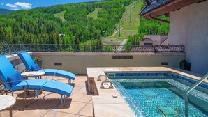 A rooftop terrace with a swimming pool, lounge chairs, and a scenic view of a forested mountain.