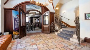 A spacious lobby with a stone floor, a grand staircase with ornate metal railings, and a chandelier.