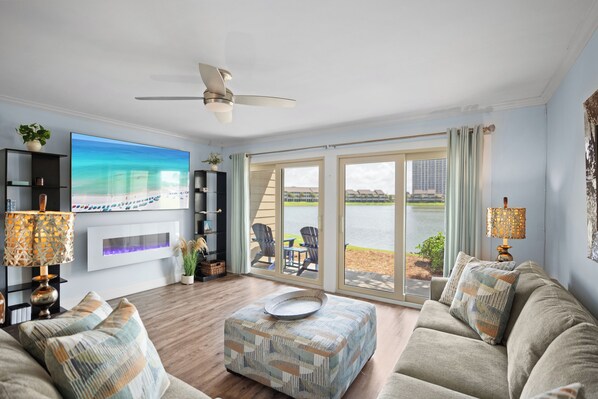 A living room with a large TV, a ceiling fan, and a view of the outdoors through sliding glass doors.