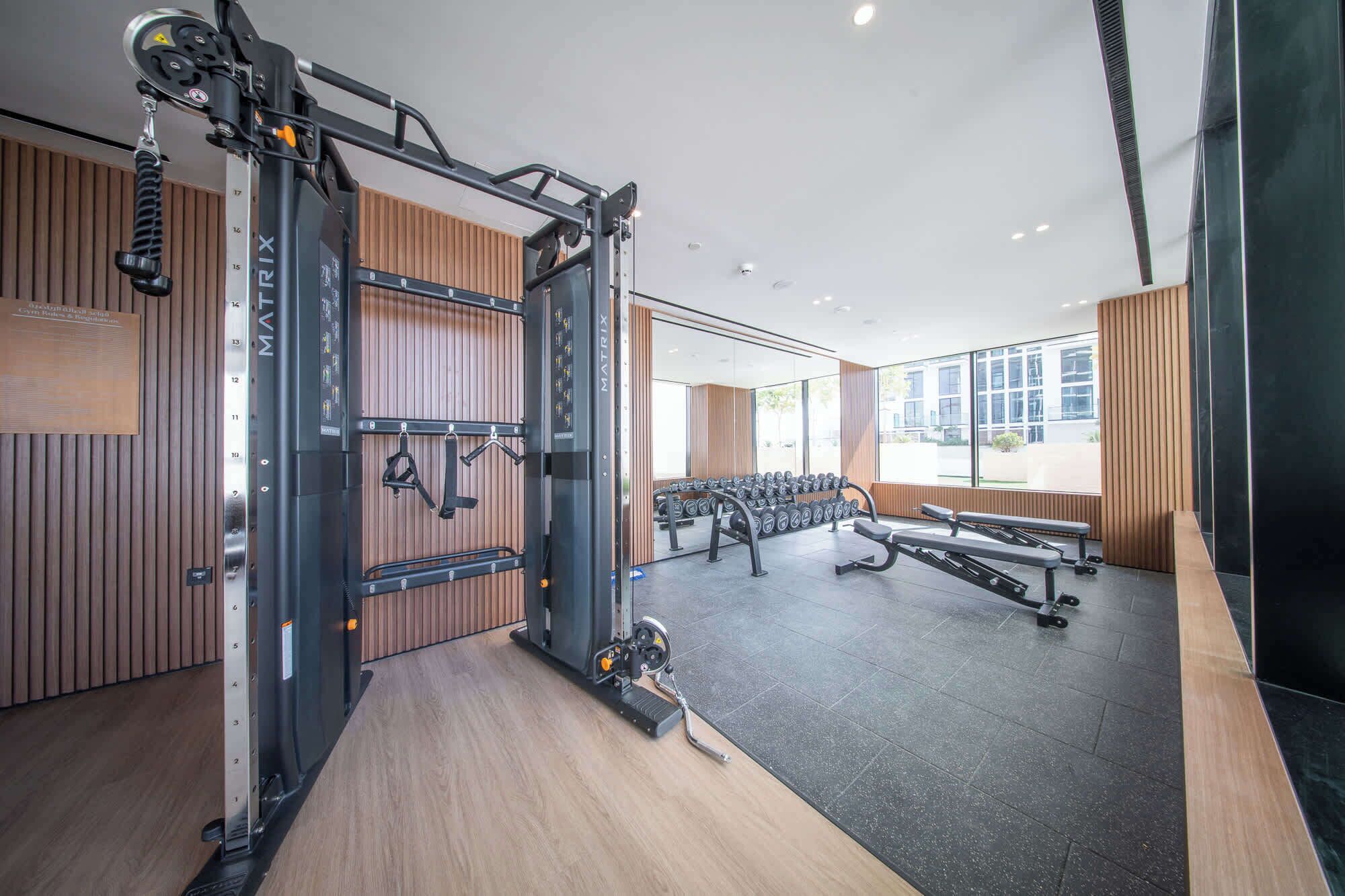 Un gimnasio moderno con equipamiento de levantamiento de pesas, bancos y un muro espejado.
