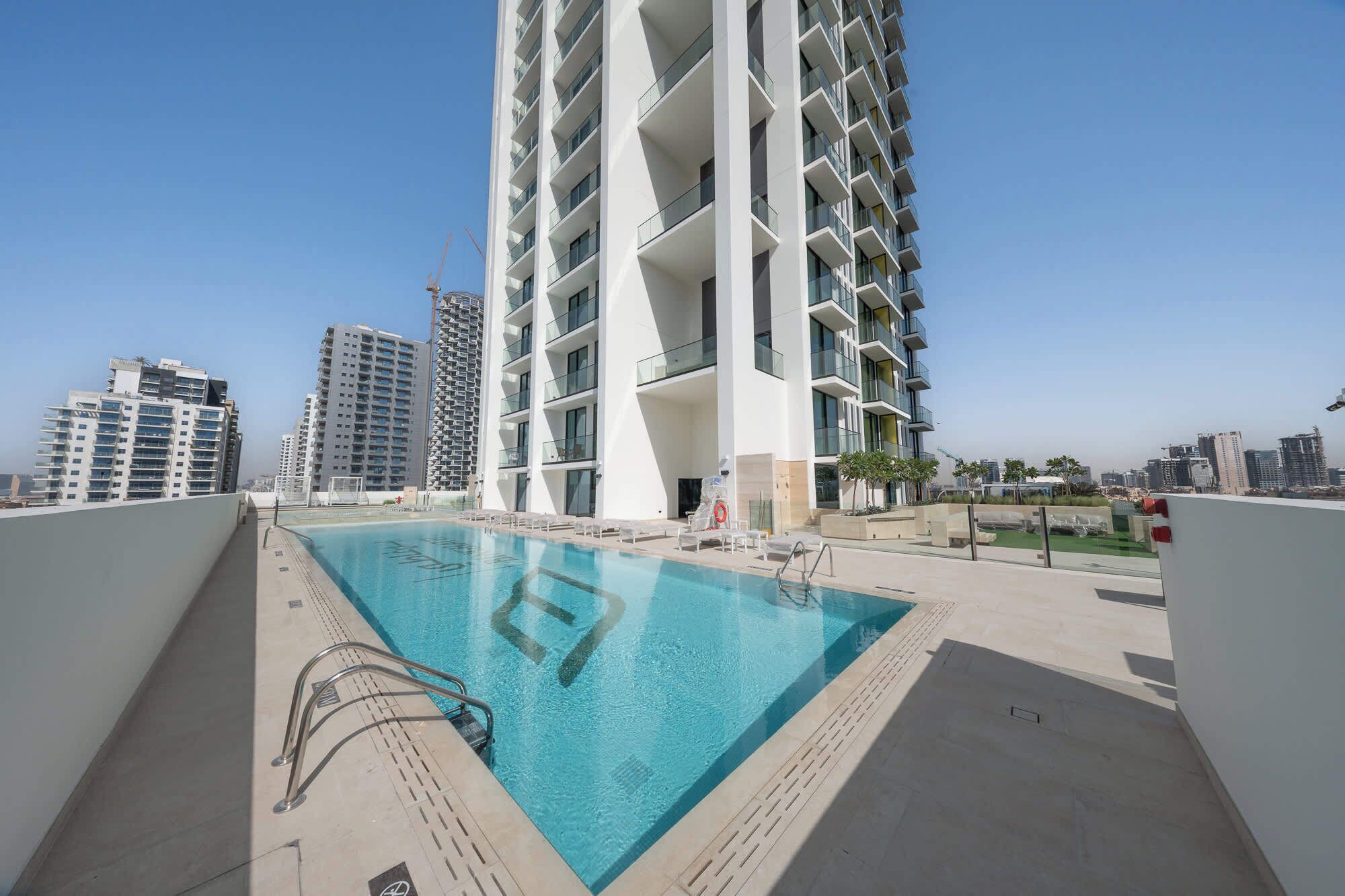 Un immeuble d’appartements moderne doté d’une piscine sur le toit, entouré d’autres immeubles de grande hauteur.
