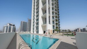 A modern apartment building with a rooftop pool, surrounded by other high-rise buildings. - StayShort - Luxury 1-Bedroom JVC Apartment with Balcony & Pool (JVC)