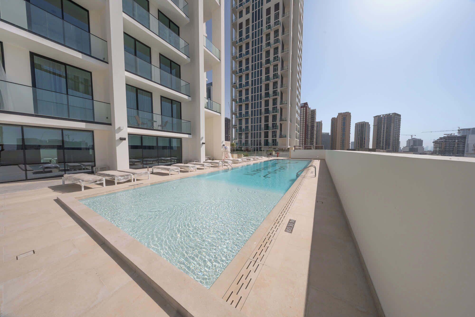 A rooftop pool with lounge chairs, a clear view of the city skyline, and modern high-rise buildings in the background.