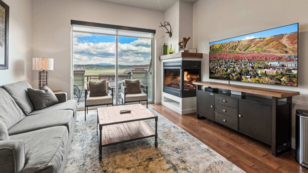 A modern living room with a fireplace, a large TV, and a scenic view through the glass doors.