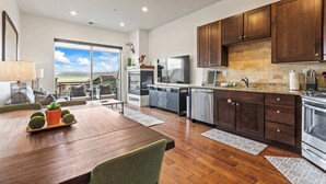 A modern kitchen with dark wooden cabinets, stainless steel appliances, and a large window offering a view of the outdoors.