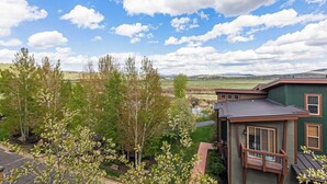 A house with a green exterior, a deck, and a view of a pond and distant hills.