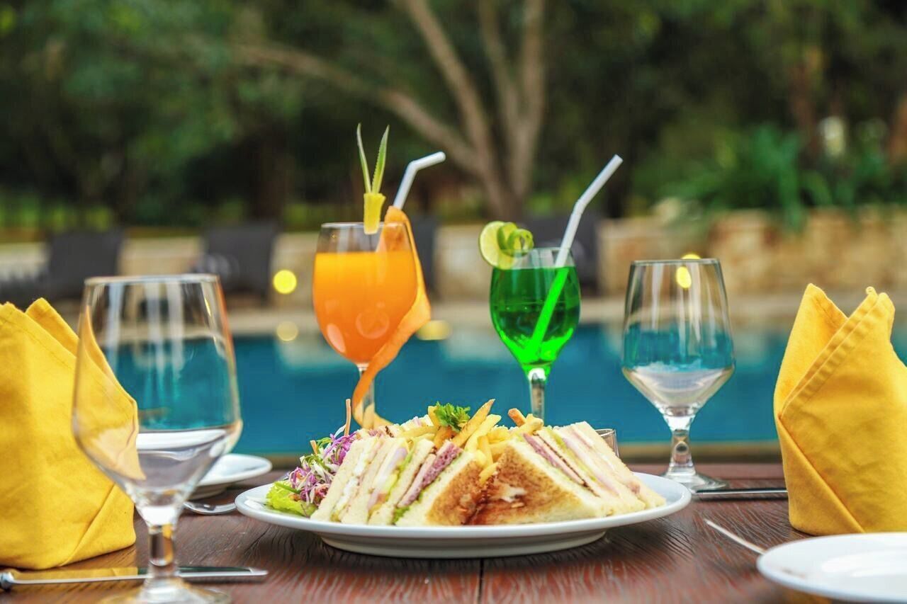 Una mesa de comedor con un plato de comida, dos vasos de jugo de naranja y dos vasos de un líquido verde, probablemente cócteles, con pajitas.