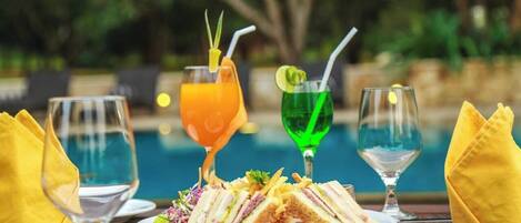 Una mesa de comedor con un plato de comida, dos vasos de jugo de naranja y dos vasos de un líquido verde, probablemente cócteles, con pajitas.
