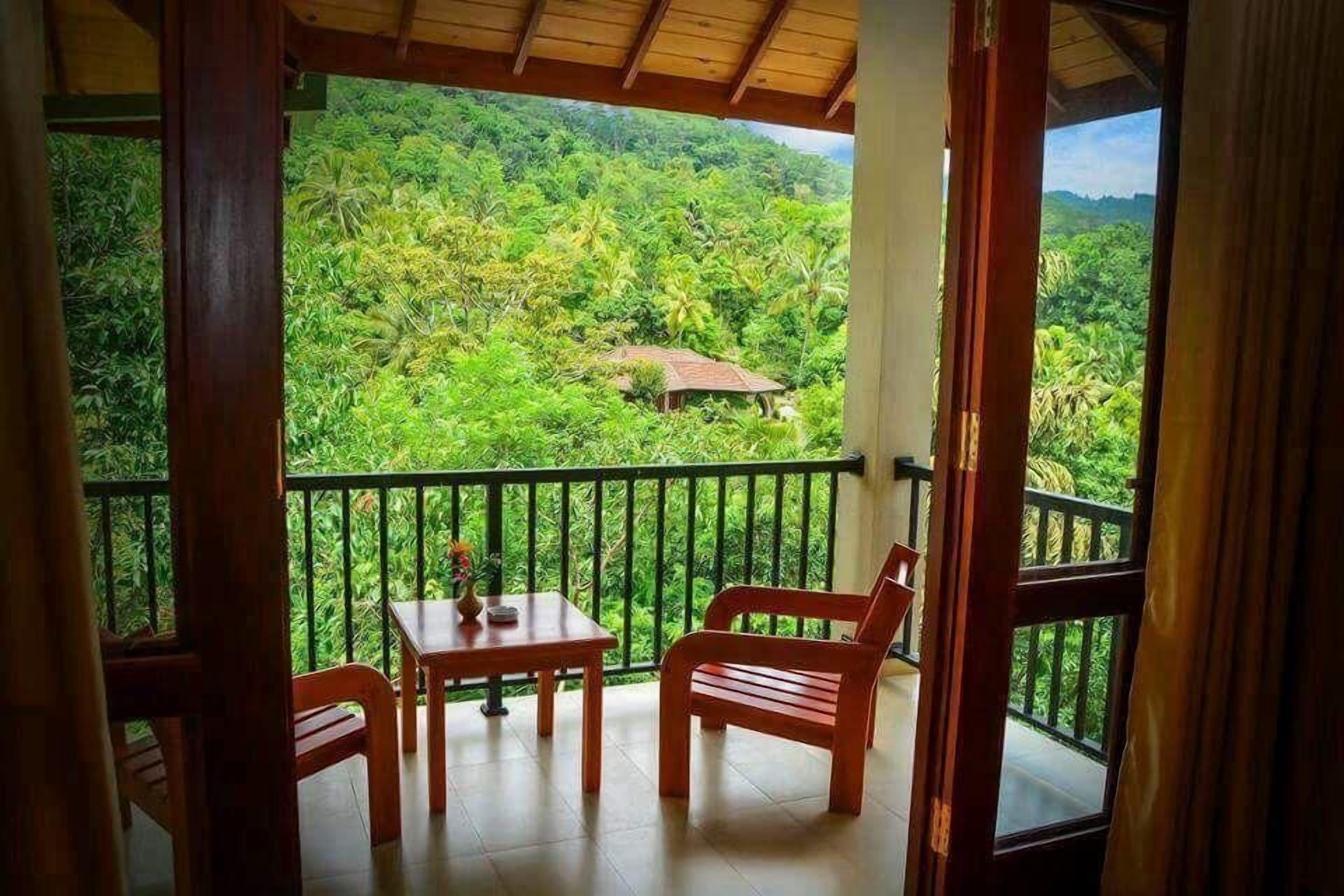 A balcony with a table and chairs, overlooking a lush green landscape with a small house in the distance.