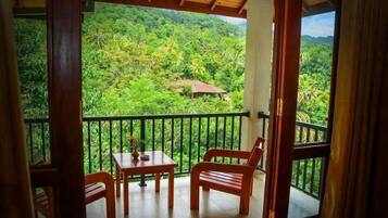 A balcony with a table and chairs, overlooking a lush green landscape with a small house in the distance.