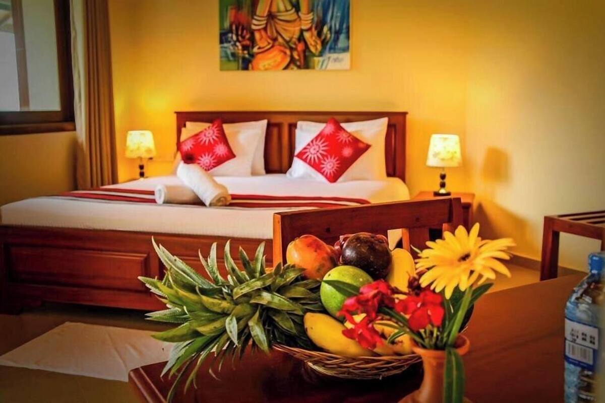 Habitación de hotel con una cama, dos lámparas de noche, una cesta de frutas y un cuadro en la pared.