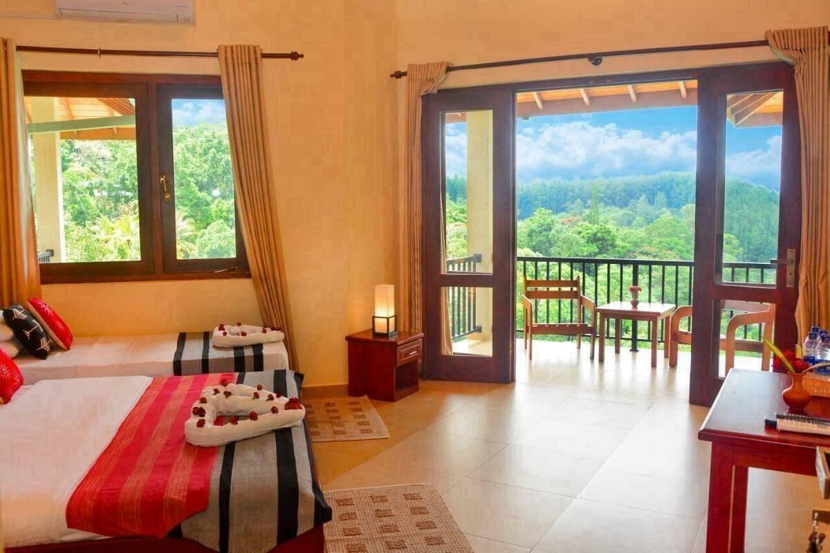 Habitación de hotel con dos camas, un balcón con mesa y sillas, y vistas al bosque.