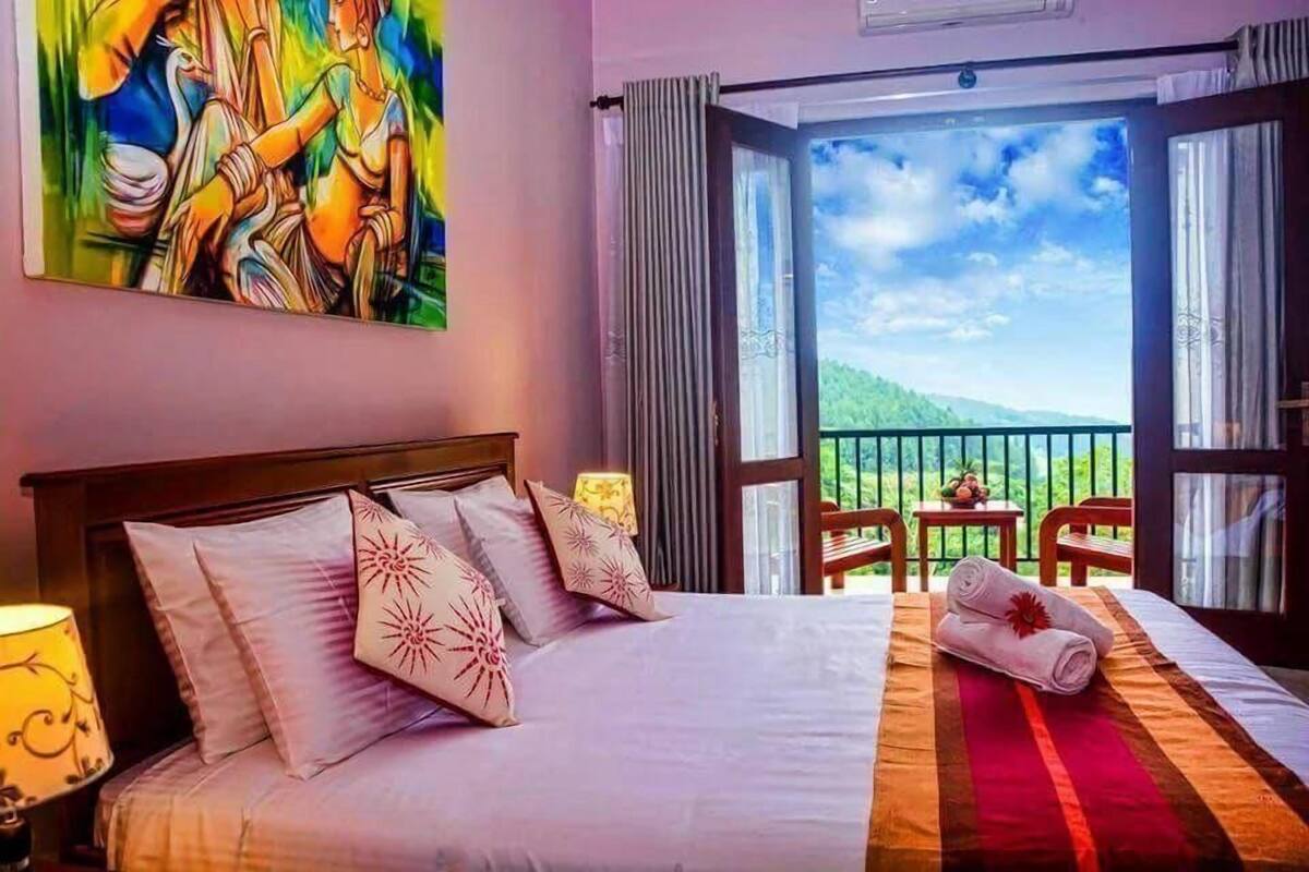Habitación de hotel con cama, un cuadro, balcón con vistas y una mesa con sillas.