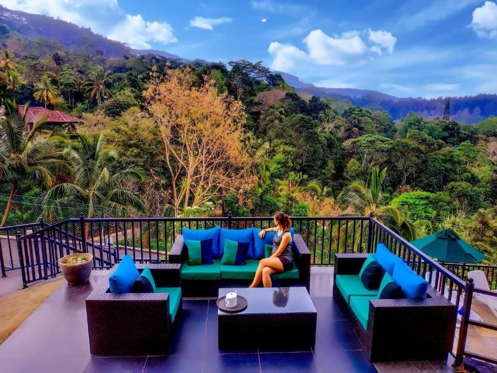 Un balcón con sofá y mesa de centro, con vistas a un paisaje exuberante con árboles y colinas.