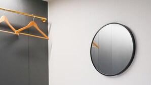 Une chambre d’hôtel moderne avec un miroir rond, une table en bois, deux tabourets en bois et un porte-vêtements.