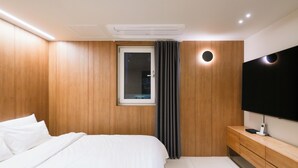 Une chambre moderne avec un mur recouvert de panneaux en bois, un lit avec une literie blanche, une table de chevet sur laquelle se trouve un téléviseur à écran plat, et une fenêtre avec des rideaux.