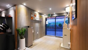 Un espace d’accueil d’hôtel au design moderne, comprenant un comptoir d’accueil, une plante en pot, une grande fenêtre offrant une vue dégagée et un panneau fixé au mur.