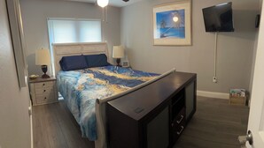 Ein Schlafzimmer mit einem Bett, Nachttischen, einem Fernseher und einem gerahmten Bild an der Wand.