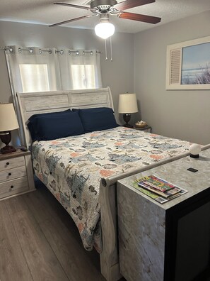 A bedroom with a bed, bedside tables, a desk, a ceiling fan, and a window with curtains.