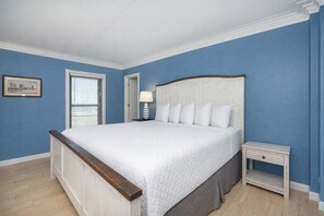 A bedroom with a large bed, a nightstand, a lamp, and a framed picture on the wall. - Island Winds East 501 3 Bedroom Condo (Gulf Shores)