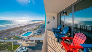 A balcony with a view of the beach and ocean, featuring blue and red Adirondack chairs and a pool. - Island Winds East 501 3 Bedroom Condo (Gulf Shores)