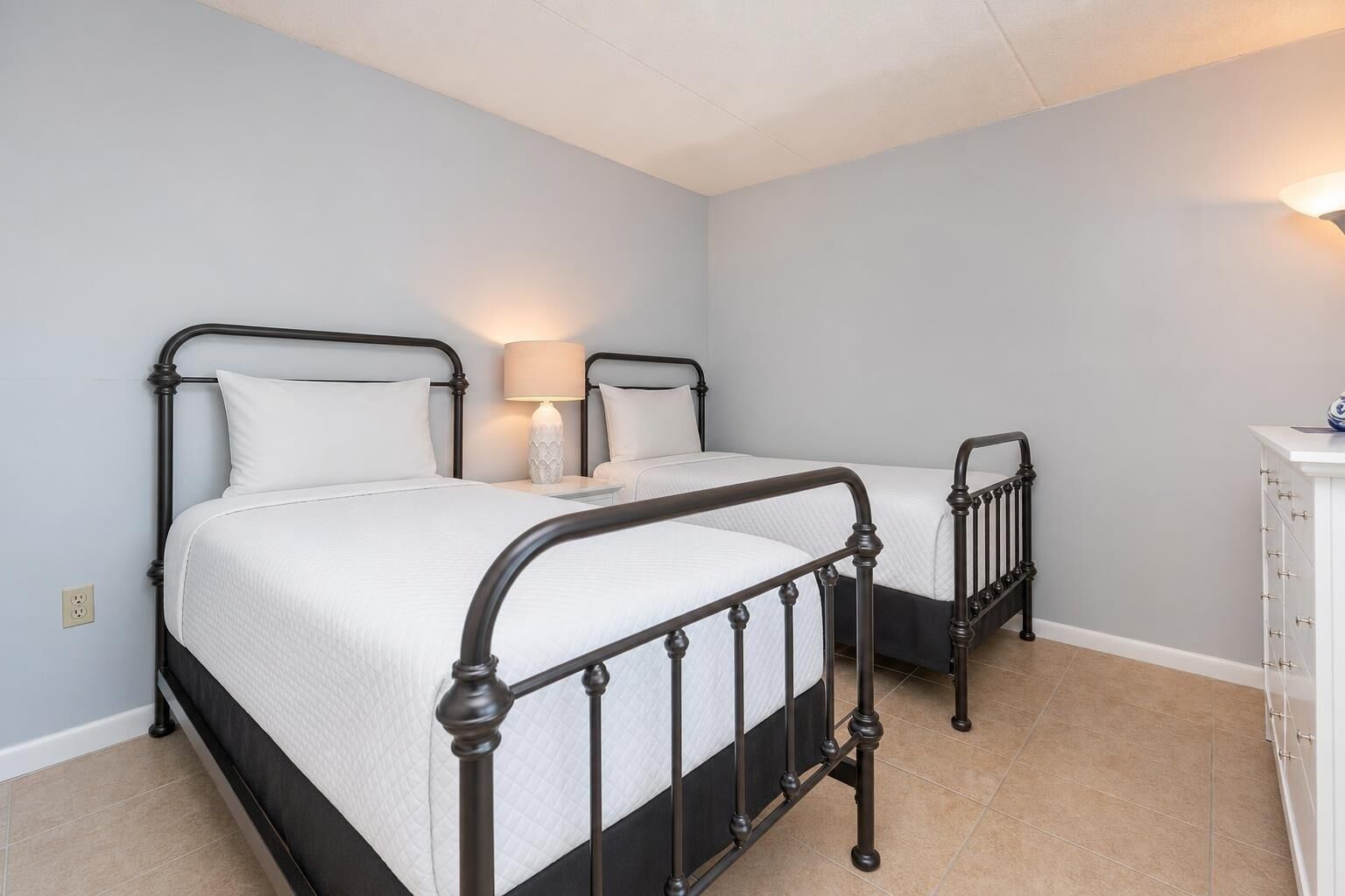 A bedroom with two beds, a bedside lamp, and a dresser.