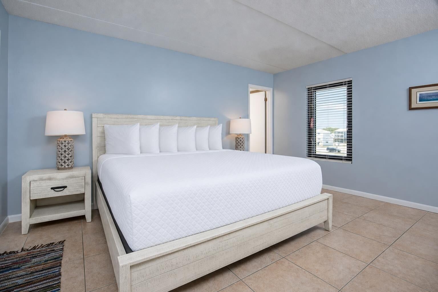 A bedroom with a bed, nightstands, a window with blinds, and a door.