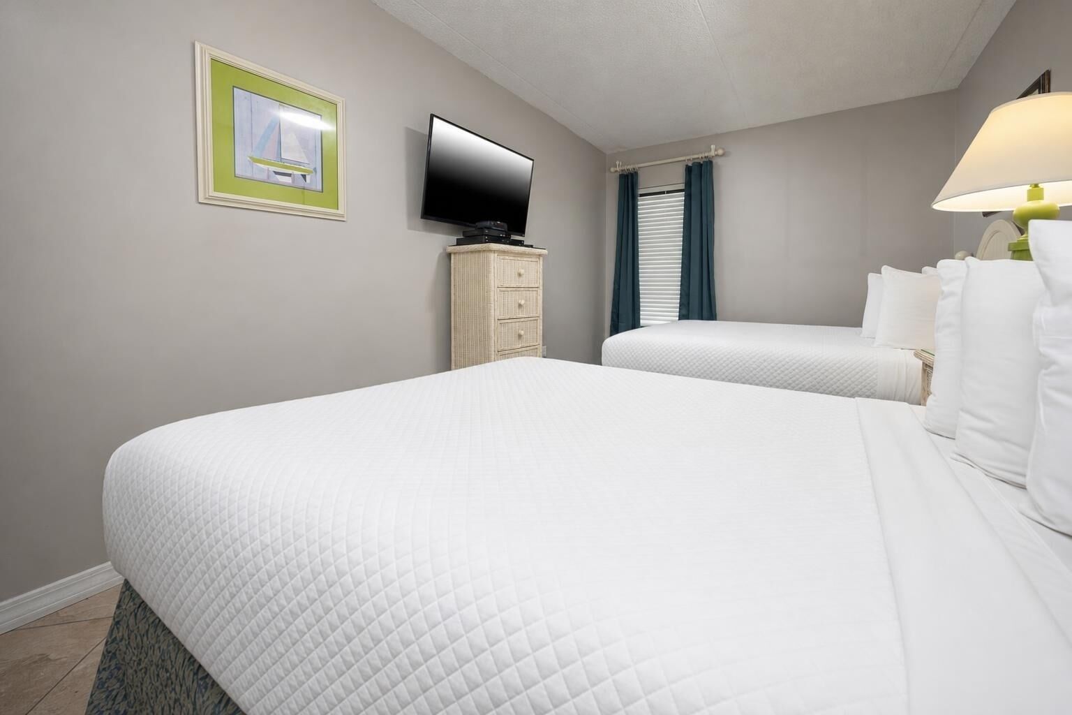 Une chambre d’hôtel avec deux lits, une télévision, une commode et une fenêtre avec des rideaux.