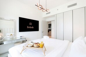 Ein modernes Hotelzimmer mit Bett, Nachttisch und einem Frühstückswagen mit Müsli, Obst und Saft.