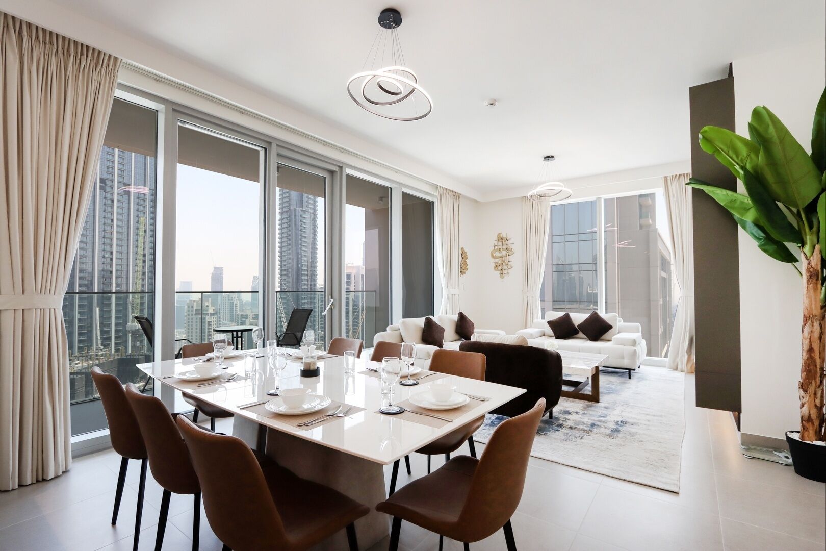 Uma área de jantar moderna com uma mesa grande posta para seis pessoas, grandes janelas com vista para a cidade e uma varanda com vista para edifícios altos.