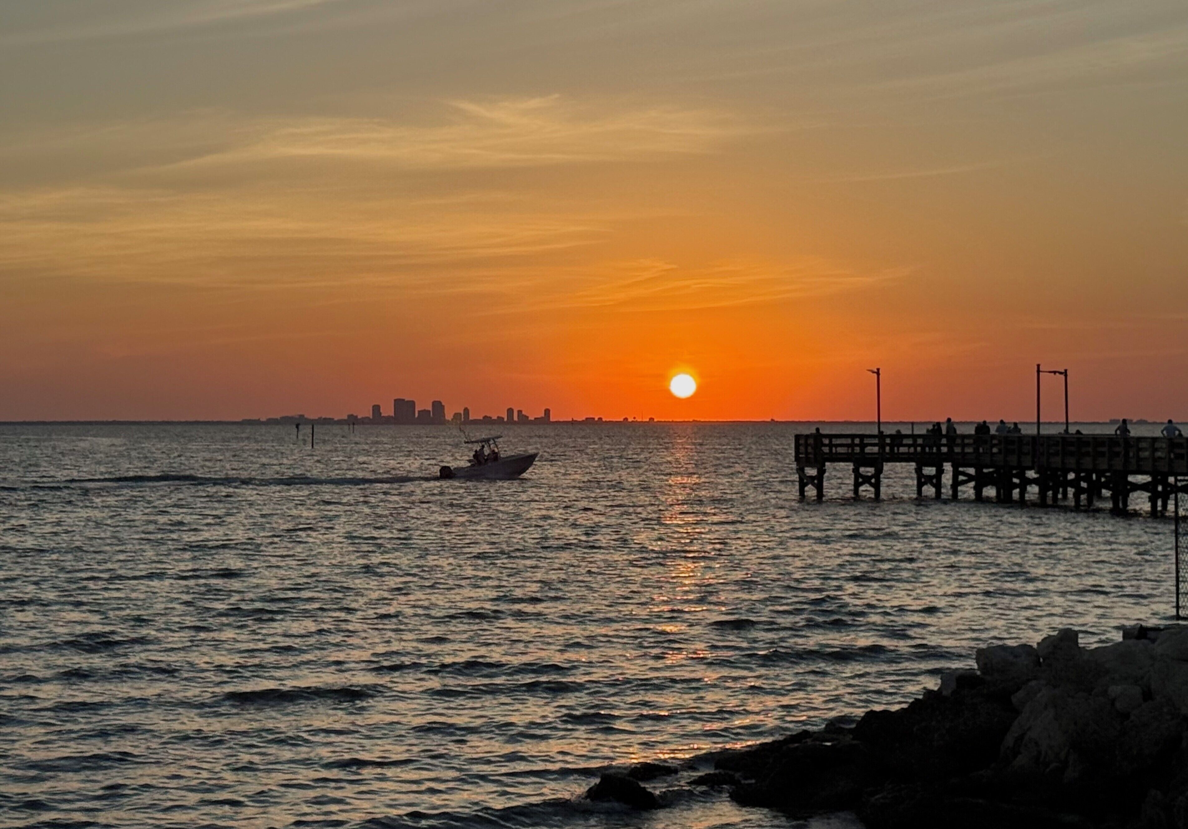 Un coucher de soleil sur une étendue d’eau, avec une jetée et un bateau.
