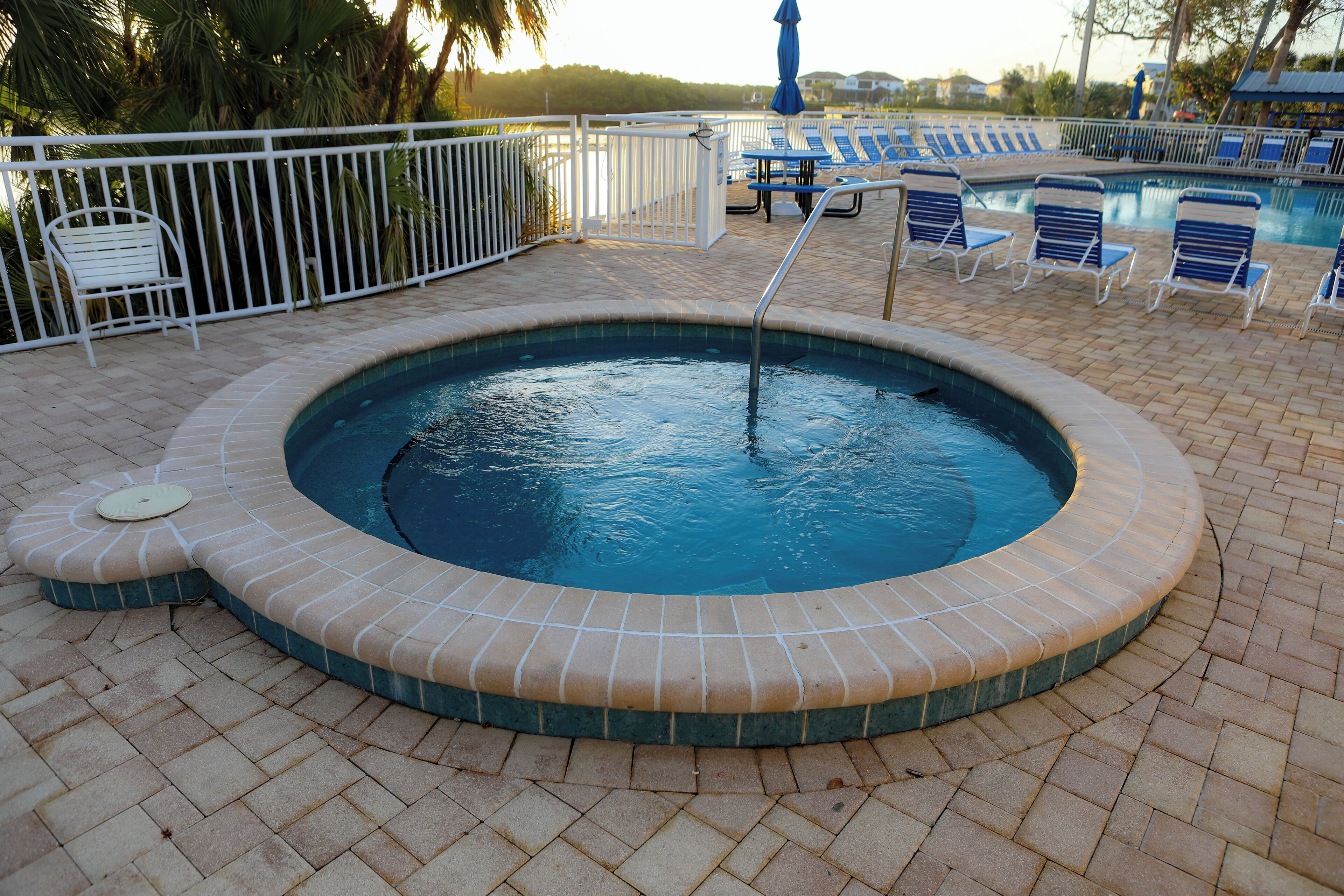 Une piscine dont le bord est recouvert de carrelage, entourée de chaises longues et d’une clôture blanche.