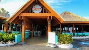 Een gebouw met een bord waarop 'Sunset Bar & Grill' staat en een rieten dak.