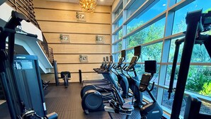 Een sportschool met trainingsapparatuur, grote ramen en een kroonluchter.