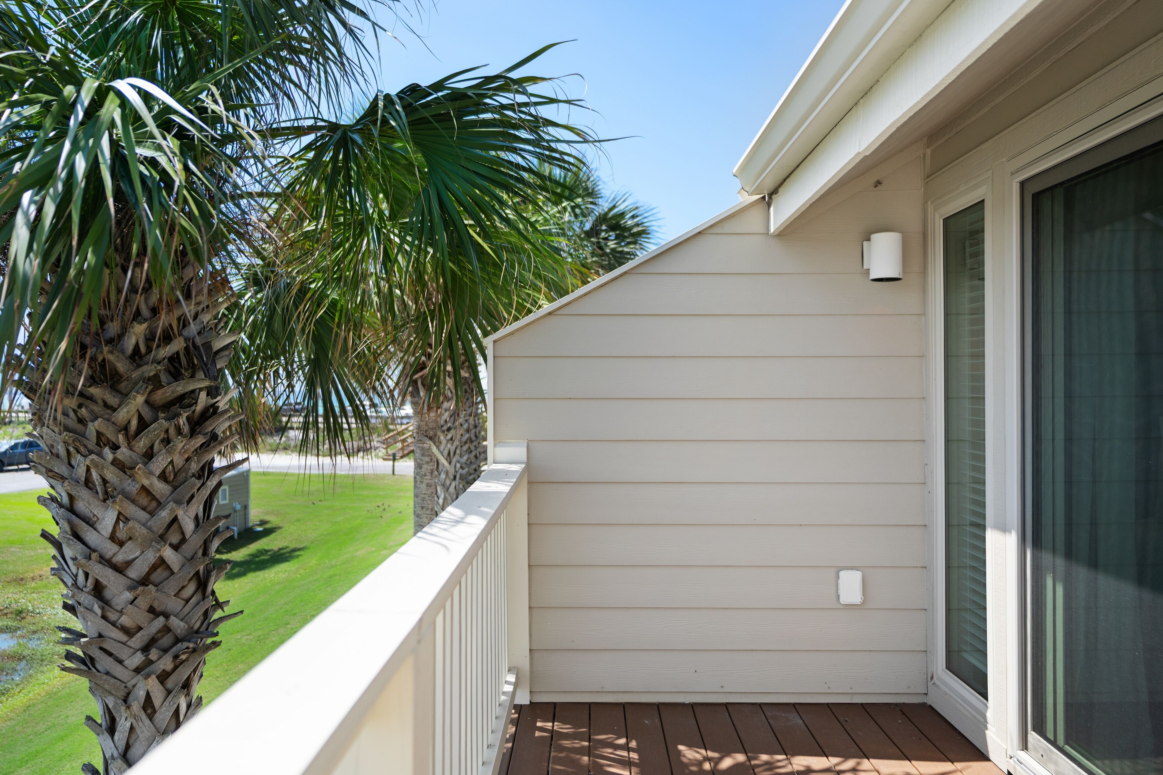 A balcony with a white railing, a palm tree, and a house with a window and a door.