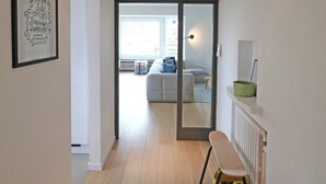 Een hal met een houten vloer, een gekaderd kunstwerk aan de muur, een bankje en een radiator.