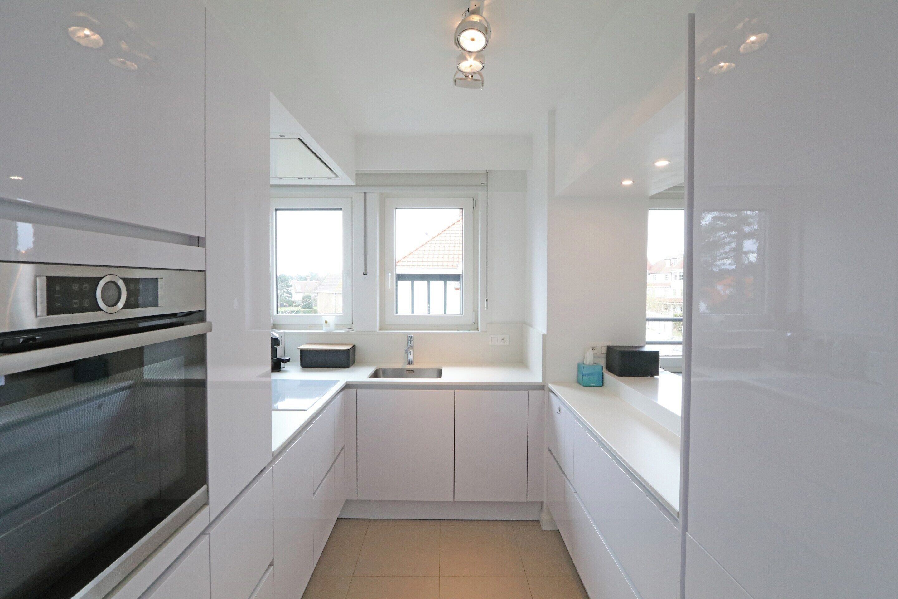A modern kitchen with white cabinetry, a built-in oven, a window, and a sink.