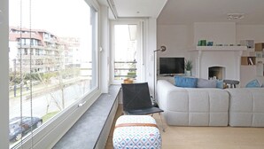 Een moderne woonkamer met een groot raam, een bank, een televisie en een open haard.