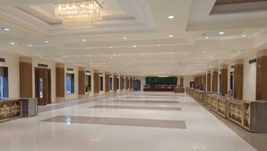 A spacious hotel lobby with a chandelier, a reception desk, and a stage in the background.