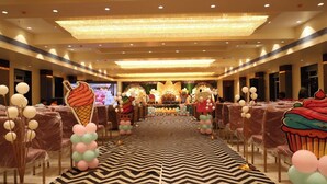 Une salle de banquet dotée d’une scène centrale, de rangées de chaises et d’un tapis à motifs.