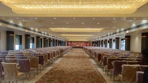 Une grande salle, bien éclairée, avec des rangées de chaises et une scène centrale, ce qui laisse supposer qu’il s’agit d’un espace dédié aux conférences ou aux événements.