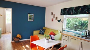 A modern kitchen with a dining area, a sofa, and a window with a view of greenery. - The Hide - A Secret Cabin in the Trees: Peace Nature & Privacy! (Tiverton)