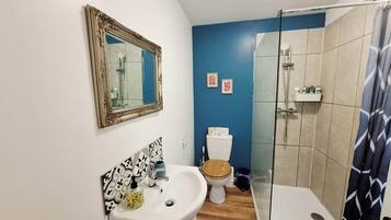 Une salle de bain avec un lavabo blanc, des toilettes avec un abattant en bois, une douche avec une porte en verre et un mur bleu.