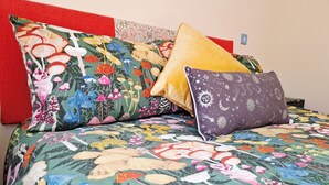 A bed with a colorful floral bedspread and multiple pillows, including a yellow one and a purple one with a moon and star pattern. - The Hide - A Secret Cabin in the Trees: Peace Nature & Privacy! (Tiverton)